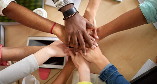 Photo of multiethnic hands on top of each other symbolizing community and teamwork.